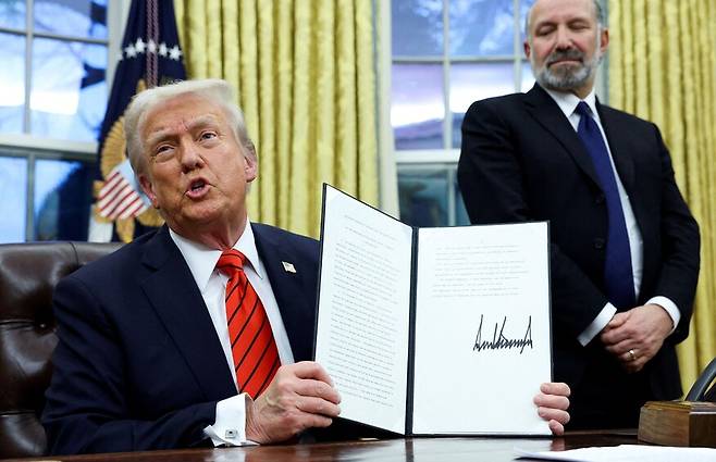 도널드 트럼프 미국 대통령(앞)이 10일(현지시각) 워싱턴 백악관 집무실에서 하워드 러트닉 상무장관 지명자(뒤)가 지켜보는 가운데 미국으로의 철강 수입 관세를 조정하는 포고문을 들어 보이고 있다. 워싱턴/AP 연합뉴스