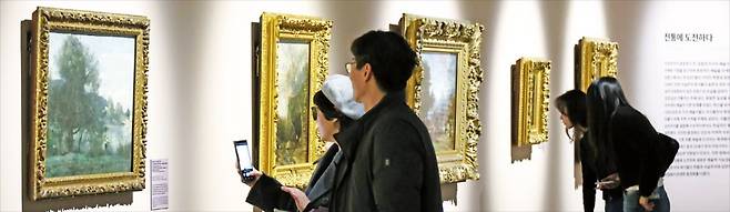 ‘인상파, 모네에서 미국으로: 빛, 바다를 건너다’ 특별전 개막을 하루 앞둔 14일 사전 공개 행사로 전시회를 찾은 방문객들이 장 바티스트 카미유 코로의 풍경화 ‘빌 다브레의 목가적 장소-연못가의 어부’(맨 왼쪽) 등의 작품을 감상하고 있다. 최혁 기자