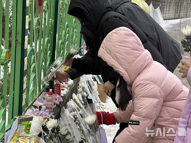 [대전=뉴시스] 김도현 기자 = 지난 12일 오후 초등학생 피살 사건이 발생한 대전 서구 관저동의 한 초등학교 정문 옆 담장에서 김하늘(7)양을 추모하는 아이와 부모가 꽃을 내려놓고 있다. 2025.02.12. kdh1917@newsis.com