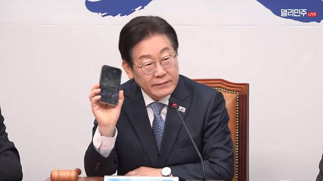 이재명 더불어민주당 대표가 26일 오전 열린 최고위원회의에서 휴대전화를 꺼내들어 보이고 있다. /민주당 유튜브 '델리민주' 채널