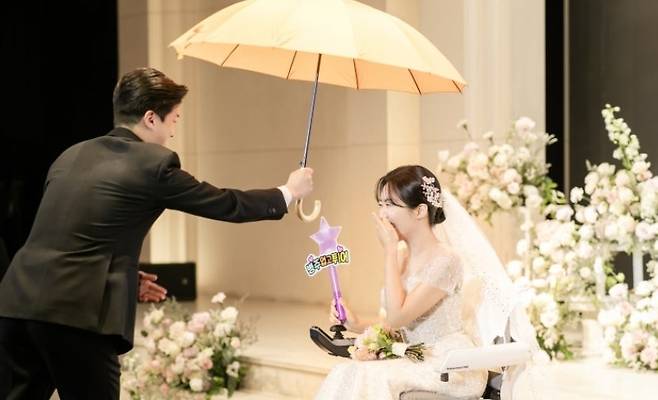 Mimicking a scene from the TV drama "Lovely Runner," groom Jeon Byung-ju (left) shields bride Kim Hye-mi with a yellow umbrella during their wedding in June last year. (Kim Hye-mi)
