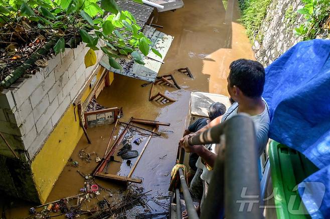 3일(현지시간) 자카르타 페하텐 바라트 지역에서 밤사이 내린 폭우로 침수된 후 사람들이 인양된 소지품을 들고 높은 지대에 서 있다. 2025.3.6 ⓒ AFP=뉴스1