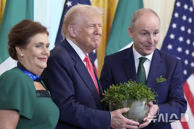 [워싱턴=AP/뉴시스] 도널드 트럼프(오른쪽) 미국 대통령이 12일(현지 시간) 백악관 이스트룸에서 열린 아일랜드 국화 '샴록' 전달 행사 중 미할 마틴 아일랜드 총리 내외와 샴록 화분을 들고 포즈를 취하고 있다. 트럼프 대통령은 "아일랜드에는 500만 명이 살고 있지만, 미국에는 아일랜드계 후손 3,500만 명이 살고 있다"라며 양국 간의 유대를 강조했다. 2025.03.13.