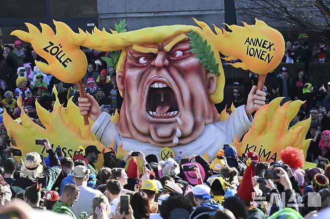 [뒤셀도르프(독일)=AP/뉴시스]지난 3일 독일 뒤셀도르프에서 열린 전통적 로즈 카니발 퍼레이드에 불꽃에 둘러싸인 도널드 트럼프 미 대통령을 묘사한 카니발 수레 주변에 '병합, 관세, 기후 파괴, 대량 추방'이라는 문구가 쓰여 있다. 트럼프의 관세 부과에 반발, 유럽에서도 미국산 제품을 사는 대신 프랑스와 유럽 제품 구매에 나서늠 미국 제품 보이콧 운동이 일고 있다고 프랑스24가 14일(현지시각) 보도했다. 2025.03.15.