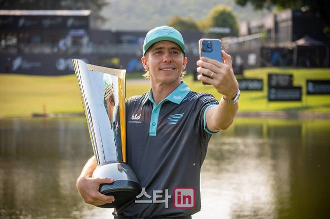 카를로스 오르티스가 우승트로피를 든 채 휴대전화로 사진을 찍고 있다. (사진=아시안투어)