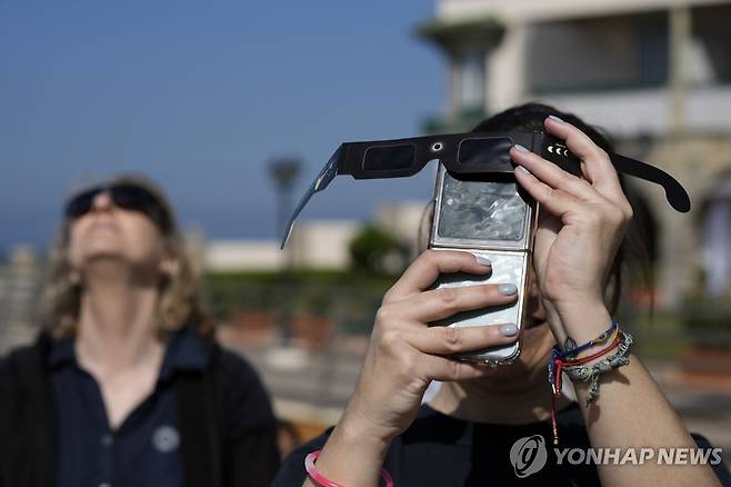 부분 일식 촬영하는 사람들 (리스본 AP=연합뉴스) 29일(현지시간) 포르투갈 리스본에서 한 여성이 카메라에 선글라스를 갖다 댄 채로 부분 일식을 촬영하려 하고 있다. 2025.03.30