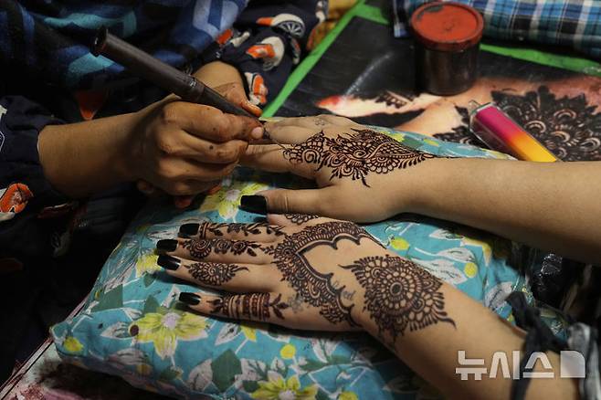 [라호르=AP/뉴시스] 30일(현지 시간) 파키스탄 라호르에서 미용사들이 라마단 성월의 끝을 알리는 이드 알피트르를 맞아 여성 고객들의 손에 전통 '헤나' 문신을 그려주고 있다. 2025.03.31.