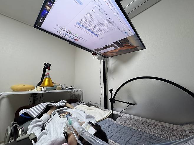 Lying in bed with a ventilator, Jang Ik-seon uses his custom-mounted monitor and eye-tracking system to write, game, and advocate for disability rights. (Moon Joon-hyun/The Korea Herald)