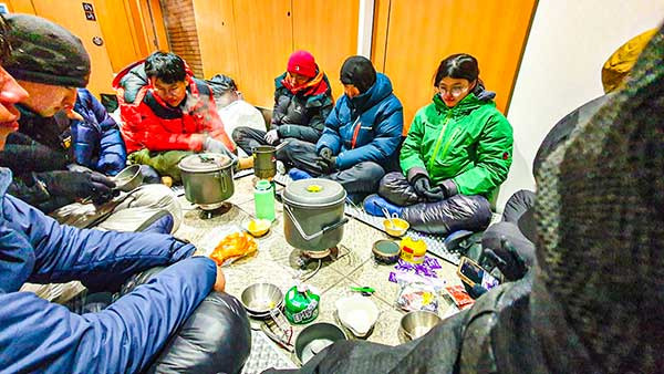저녁을 먹기 위해 다 함께 화장실 바닥에 둘러앉았다. 한쪽에서는 마실 물을 만들기 위해 눈을 끓이고 있고, 다른 한쪽에서는 밥을 짓고 있다.