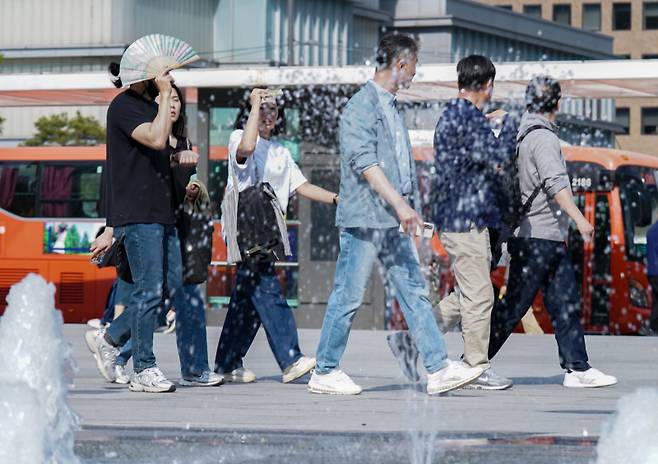 서울 종로구 광화문광장 분수대에서 시민들이 햇빛을 가리며 이동하고 있다. 유희태 기자