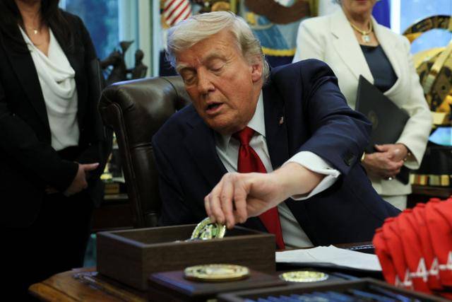 도널드 트럼프 미국 대통령이 24일 워싱턴 백악관 집무실에서 퇴역 군인들에게 건네줄 메달 모양 주화를 집어들고 있다. 워싱턴=로이터 연합뉴스