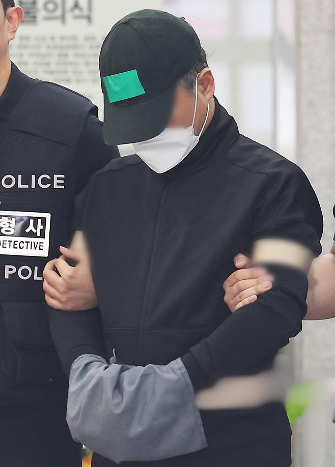 The suspect accused of killing his parents, his wife and two daughters is escorted out of the Yongin Seobu Police Station by police officers in Gyeonggi Province on Thursday. (Yonhap)