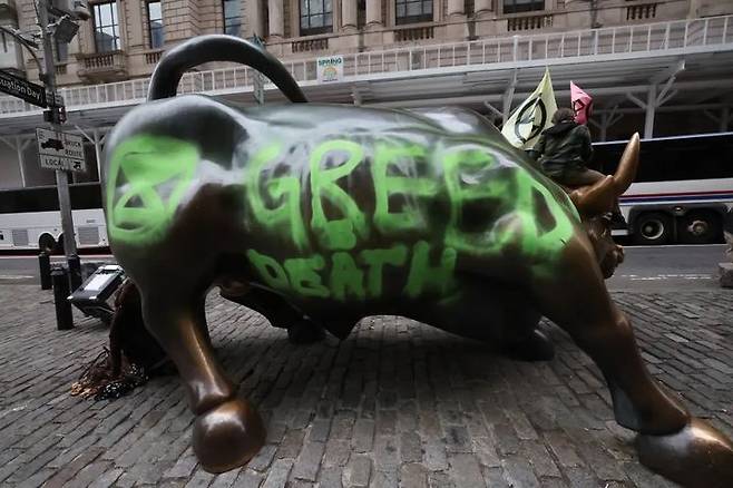 [서울=뉴시스] 22일 기후환경 단체인 '멸종 반란'의 회원 일부가 월가의 돌진하는 황소를 훼손하며 시위를 벌였다. 단체의 상징 문양과 "GREED=DEATH" 문구를 적어놓은 모습. (사진=뉴욕포스트) 2025.04.23. *재판매 및 DB 금지