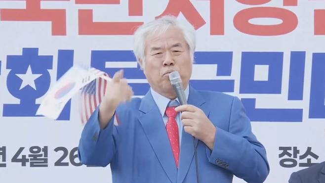 26일 광화문 집회 연단에 오른 전광훈 목사가 태극기를 흔들며 발언하고 있다. 그는 2년 내 자유통일과 윤석열 전 대통령 복귀를 주장했다. (‘전광훈TV‘ 캡처)