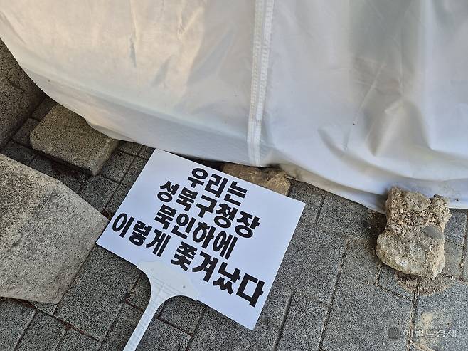 25일 오전 8시께 서울 성북구 성북구청 앞에 ‘우리는 성북구청장 묵인하에 이렇게 쫒겨났다’다‘는 문구가 적힌 손팻말이 놓여있다. 김도윤 기자.