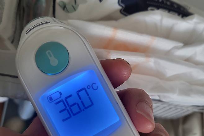 아이의 체온을 측정하는 디지털 체온계. 부모들은 자녀의 체온 변화에 민감하게 반응하며, 응급 상황을 대비해 병원 접근성을 고려하게 된다.