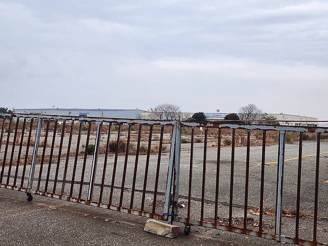 지난 2018년 폐쇄된 후 매각된 옛 한국GM 군산공장의 출고 대기장. 굳게 닫힌 녹슨 철문 뒤로 잡초가 무성한 빈 땅과 멀리 빛바랜 쉐보레 로고가 보인다. /진상훈 기자