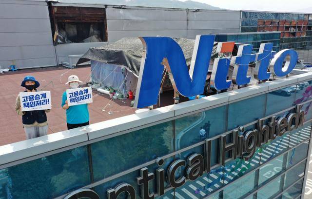 10일 경북 구미시 한국옵티칼하이테크 고공농성장에서 박정혜(왼쪽), 소현숙 노동자가 손팻말을 들고 있다. 뒤로는 불타버린 공장이 그대로 남아있다. 구미=홍인기 기자
