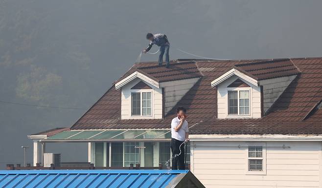 28일 오후 2시 1분쯤 대구 북구 노곡동 함지산에서 산불이 발생한 가운데 주민들이 주택 지붕에 물을 뿌리고 있다. /연합뉴스