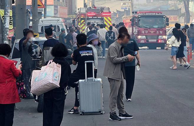 28일 대구 북구 노곡동 경부고속도로 북대구 나들목(IC) 인근 함지산 자락에서 산불이 발생해 연기가 시내까지 확산하자 인근 주민들이 대피하고 있다. 여행용 가방에 짐을 챙겨 나온 주민들이 마스크를 쓰고 있고, 뒤에는 소방차가 진입하고 있다. 대구 도심에서 대형 산불이 발생한 것은 1990년 이후 35년 만이다. 대구=뉴시스