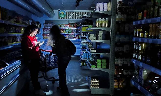 28일(현지시각) 스페인 바르셀로나의 한 슈퍼마켓에서 정전으로 불이 꺼진 가운데 한 직원이 손전등 불빛에 의존해 고객을 돕고 있다. 로이터 연합뉴스