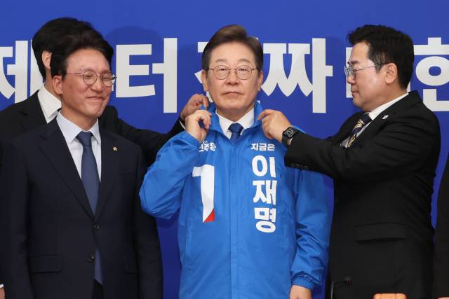 ▲더불어민주당 박찬대 당대표 직무대행 겸 원내대표가 지난 28일 서울 여의도 국회에서 열린 최고위원회의에서 이재명 대선 후보에게 선거운동용 파란색 점퍼를 입혀주고 있다. ⓒ연합뉴스