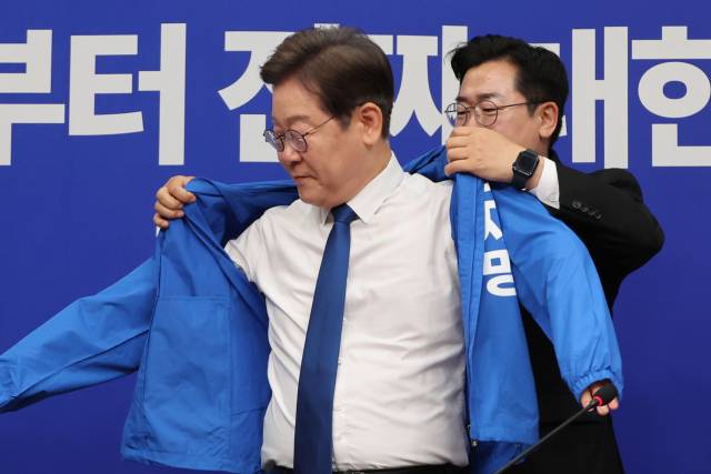 더불어민주당 박찬대 당대표 직무대행 겸 원내대표가 28일 서울 여의도 국회에서 열린 최고위원회의에서 이재명 대선 후보에게 선거운동용 파란색 점퍼를 입혀주고 있다. 연합뉴스