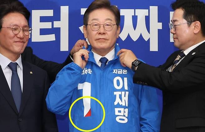 더불어민주당 박찬대 당대표 직무대행 겸 원내대표(오른쪽)가 지난 28일 서울 여의도 국회에서 열린 최고위원회의에서 이재명 대통령 후보에게 선거운동용 파란색 점퍼를 입혀주고 있다. 노란색 원 안에 빨간 세모가 보인다. 연합뉴스