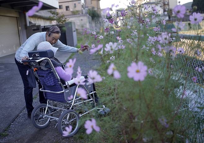 일본 도쿄에 있는 요양원 인근에서 70대인 에이이치 오쿠보 씨가 치매를 앓고 있는 60대 아내 유미코씨에게 꽃을 가리키며 얘기하고 있다. 일본의 치매 환자가 약 600만명에 달하는 가운데 이들의 자산을 확인하지 못해 묶여버린 ‘치매머니’가 2017년 기준 143조엔(약1427조원)에 달해 사회적 문제가 되고 있다  [로이터]