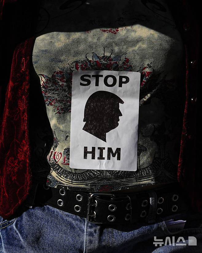 [뉴욕=AP/뉴시스] 지난 17일(현지 시간) 미국 뉴욕 폴리 광장에서 열린 '고등교육 행동의 날' 시위 중 한 시민이 도널드 트럼프 대통령 옆모습이 그려진 스티커를 셔츠에 붙이고 있다. 2025.04.30.