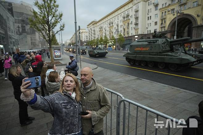 [모스크바=AP/뉴시스] 29일(현지 시간) 러시아 모스크바 크베르사카야 거리에서 시민들이 전승절 군사 퍼레이드 예행연습을 하는 군용 차량을 배경으로 셀카를 찍고 있다. 러시아는 5월 9일 제2차 세계대전 승전 80주년(전승절)을 맞는다. 2025.04.30.