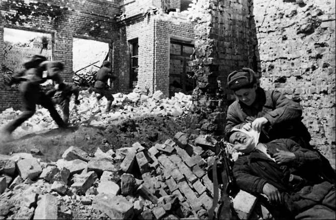 스탈린그라드 전투 당시 독일군과 시가전을 벌이는 소련군 병사들 옆에서 의무병이 부상자를 치료하고 있다. 위키피디아