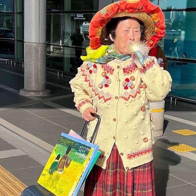 제주공항에서 피리를 불며 이륙을 기다리는 ‘그림할망’. 야광빛 스카프와 손수 만든 패랭이, 그림이 담긴 트렁크는 모두 ‘몸의 언어’다. 일상 속 예술의 출현, 선흘에서 시작한 장면이 도시를 향해 출발을 알린다. ('소셜뮤지엄’ 홈페이지)