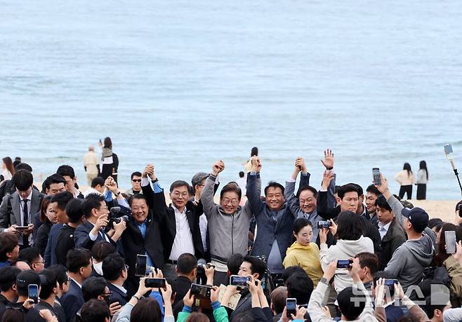 [강릉=뉴시스] 조성우 기자 = 민심을 청취하는 '경청 투어'에 나선 이재명 더불어민주당 대선후보가 3일 강원도 강릉시 안목해변 카페거리에서 이병주 의원, 이 후보 직속 이광재 국가미래정책위원회 공동위원장 등과 손을 맞잡고 주민들과 관광객들에게 인사하고 있다. 2025.05.03. xconfind@newsis.com