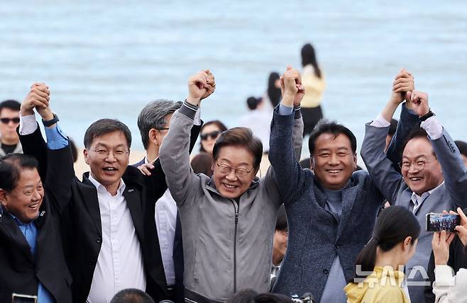 [강릉=뉴시스] 조성우 기자 = 민심을 청취하는 '경청 투어'에 나선 이재명 더불어민주당 대선후보가 3일 강원도 강릉시 안목해변 카페거리에서 이병주 의원, 이 후보 직속 이광재 국가미래정책위원회 공동위원장 등과 손을 맞잡고 주민들과 관광객들에게 인사하고 있다. 2025.05.03. xconfind@newsis.com