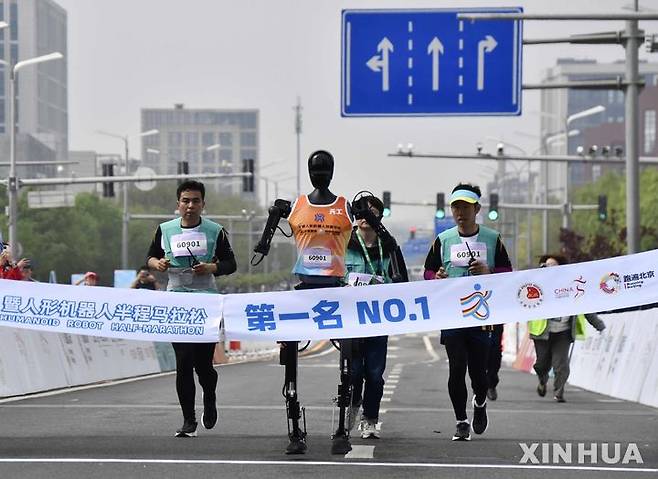 [베이징=신화/뉴시스] 19일 중국 베이징 이좡 경제기술개발구에서 열린 휴머노이드 로봇 하프마라톤에서 우승한 로봇 '톈궁 울트라'가 참가팀 인원들과 함께 달리고 있다. 2025.04.20