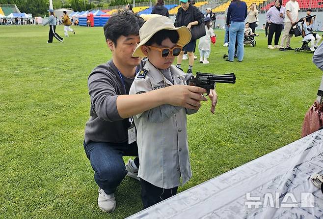[남해=뉴시스] 차용현 기자 = 5일 제103회 어린이날을 맞아   경남 남해군 스포츠파크에서 열린 ‘오늘은 나도 어린이 경찰관’이라는 경찰 체험 행사에서 한 어린이가 경찰관의 도움을 받아 모형 권총으로 사격 연습을 하고 있다. 2025.05.05.(사진=남해경찰서 제공)photo@newsis.com