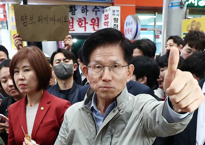People Power Party candidate Kim Moon-soo holds his thumb up while eating fishcakes in Pohang, North Gyeongsang, on May 6. One supporter in the background holds up a sign saying ″Don't yield.″ [NEWS1]