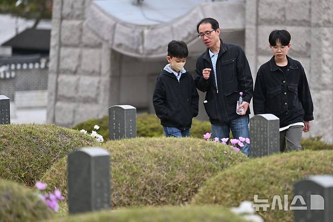 [광주=뉴시스] 이영주 기자 = 5·18민주화운동 45주기를 12일 앞둔 6일 오전 광주 북구 운정동 국립5·18민주묘지에서 한 추모객이 아들들에게 5·18 당시 숨진 희생자들의 사연을 설명해주고 있다. 2025.05.06. leeyj2578@newsis.com