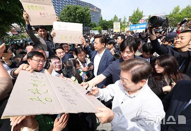 [전주=뉴시스] 조성봉 기자 = 민심을 청취하는 '경청 투어'에 나선 이재명 더불어민주당 대선후보가 7일 전북 전주시 완산구 풍남문 인근에서 공판연기를 환영하는 지지자의 응원 피켓에 사인을 해주고 있다. '공판연기 환영, 대통령은 국민이 뽑습니다'라고 적힌 피켓에 이 후보는 '맞습니다' 라고 쓰고 있다. 2025.05.07. suncho21@newsis.com