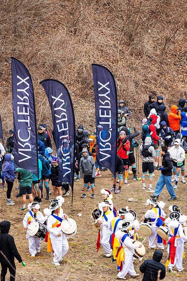 대회 둘째 날, 20km 종목 출발점인 무룡고개에 선수와 응원단이 어우러졌다. 브랜드 깃발 아래 사물놀이패가 인상적이다.&nbsp;