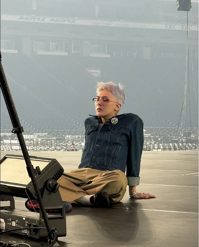 지드래곤은 단 한 개의 단추도 풀지 않은 데님 재킷을 입고 무대 바닥에 조용히 앉아 있다. 사진=지드래곤 SNS