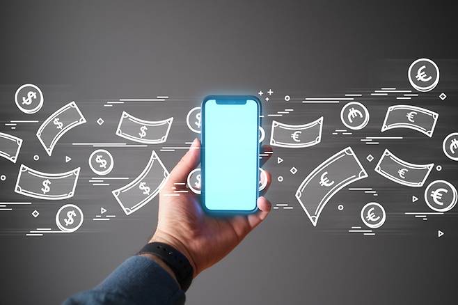 A hand is holding a mobile phone and USD dollars are entering on one side and exiting as Euro on the other.