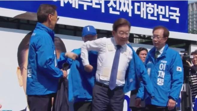 제21대 대통령선거 공식 선거운동 첫날인 12일, 서울 광화문광장에서 열린 출정식 현장에서 이재명 더불어민주당 대선 후보가 흰색 방탄복을 착용한 채 점퍼를 입고 있다. ('델리민주' 캡처)