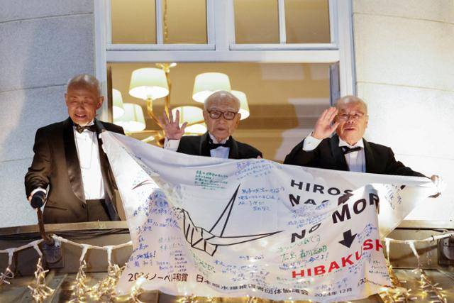일본 원자력폭탄 피해자 단체인 니혼히단쿄(일본원수폭피해자단체협의회)가 지난해 12월 10일 노르웨이 오슬로 그랜드호텔에서 열린 노벨평화상 수상 기념 횟불 행렬 행사에서 단체를 상징하는 현수막을 든 채 손을 흔들고 있다. 오슬로=로이터 연합뉴스
