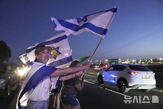 [레임=AP/뉴시스] 12일(현지 시간) 팔레스타인 무장 정파 하마스가 석방한 미국·이스라엘 이중국적 병사 에단 알렉산더가 탑승한 차량이 이스라엘 남부 레임의 군 기지에 도착하자, 미 뉴저지주 출신의 한 여성이 이스라엘 국기를 흔들며 그를 환영하고 있다. 알렉산더는 뉴저지 출신으로, 가자지구에 억류돼 있던 마지막 미국인 생존자로 알려졌다. 2025.05.13.