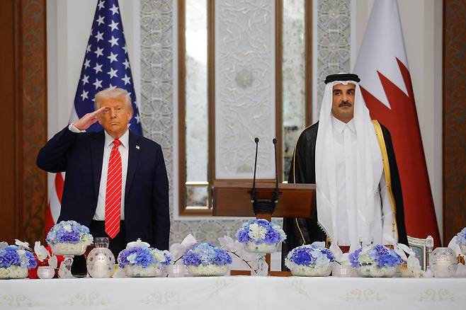 도널드 트럼프 미국 대통령이 지난 14일(현지시각) 카타르 루사일의 루사일 궁에서 열린 국빈 만찬에서 미국 국가가 연주되는 가운데 카타르의 에미르 타밈 빈 하마드 알 타니 국왕 옆에서 경례를 하고 있다. /로이터연합뉴스