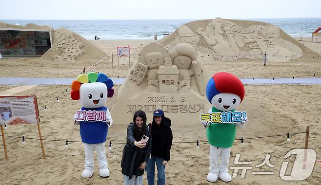 제21대 대통령선거를 앞둔 15일 오후 부산 해운대해수욕장에서 정책·공약에 대한 관심과 투표 참여를 높이기 위해 부산시선관위의 '모래로 만나는 대통령선거' 홍보 캠페인이 진행되는 가운데 외국인 관광객들이 모래작품 앞에서 셀카를 찍고 있다. 2025.5.15/뉴스1 ⓒ News1 윤일지 기자