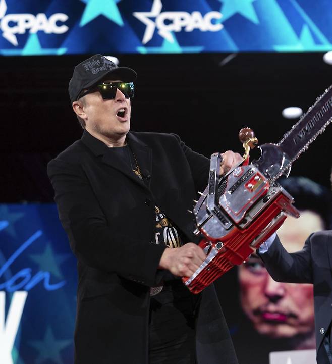 일론 머스크 정부효율부 수장 겸 테슬라 최고경영자(CEO)가 올 2월 미국 메릴랜드주 옥슨힐에서 열린 보수정치행동회의(CPAC) 행사에 등장해 전기톱을 휘두르고 있다. 당시 그는 “이 전기톱은 관료주의를 위한 것”이라고 했다. 미국 정부 안팎에선 “머스크가 연방정부 구조조정을 표현했다”는 평가가 나왔다. 옥슨힐=AP 뉴시스