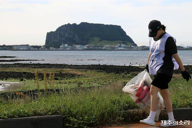 한 참가자가 해안가에서 수거한 플라스틱 쓰레기를 들고 가고 있다. 그 뒤로 제주 성산 일출봉이 우뚝 서있다.&nbsp; ⓒ제주의소리